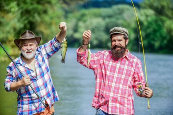 Two men hold up the small fish that they caught at a river