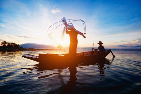 Two men begin fishing in a small boat as the sun rises