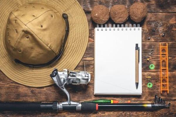 Fishing gear such as a hat, pole, notebook, and more sit on a wooden desk