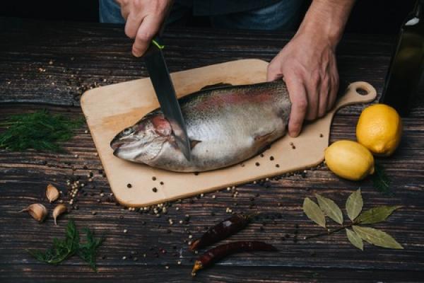 A person begins to filet a fish on a cutting board