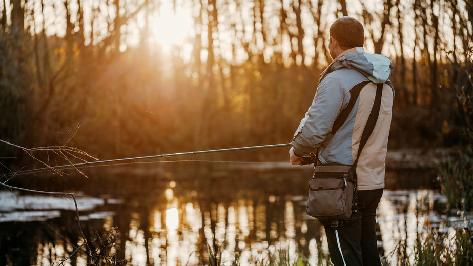 A man in a light jacket fishing on the side of a river